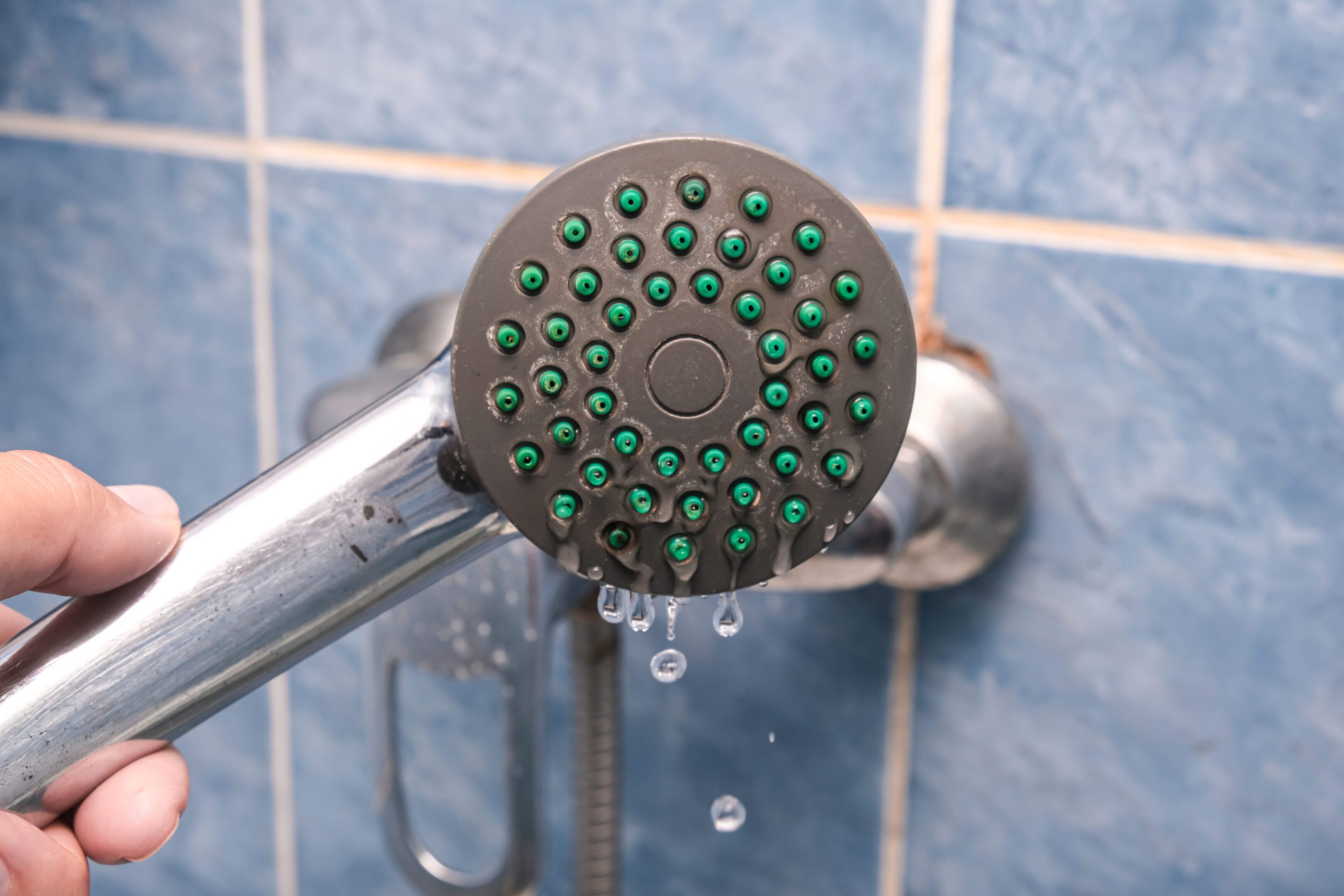 Shower head leaking water in blue-tiled bathroom