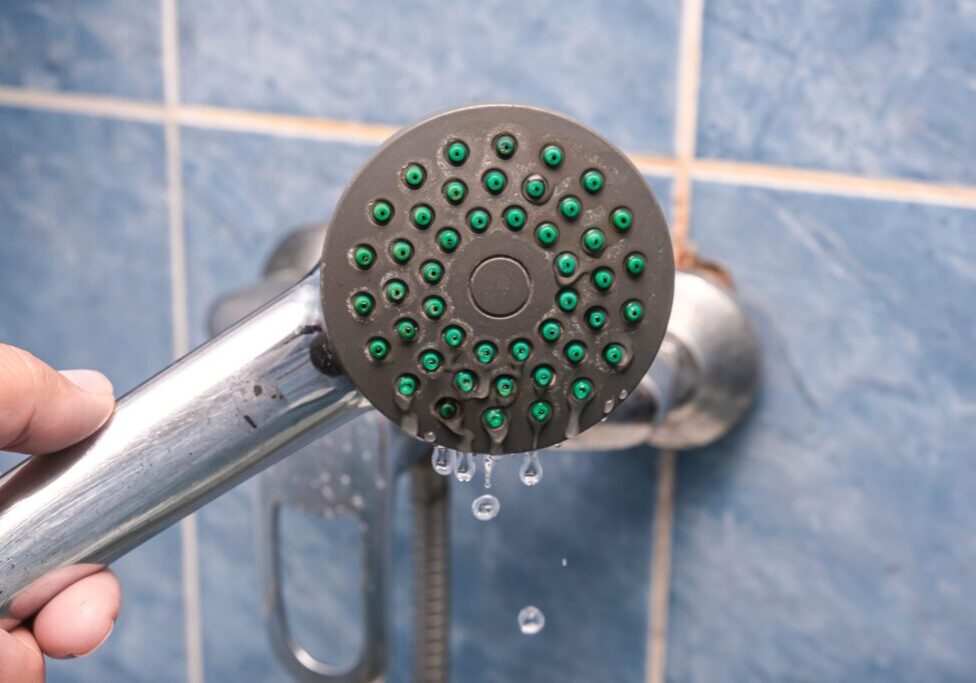 Shower head leaking water in blue-tiled bathroom